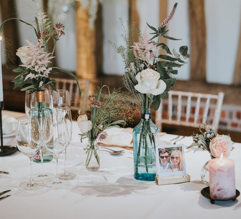 Table decor featuring personalised polaroids and florals in gin vases