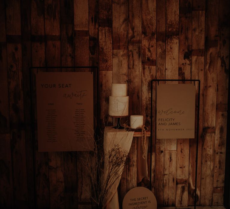 display corner with wedding welcome sign and seating chart on black frames with wedding cake and dried flowers 