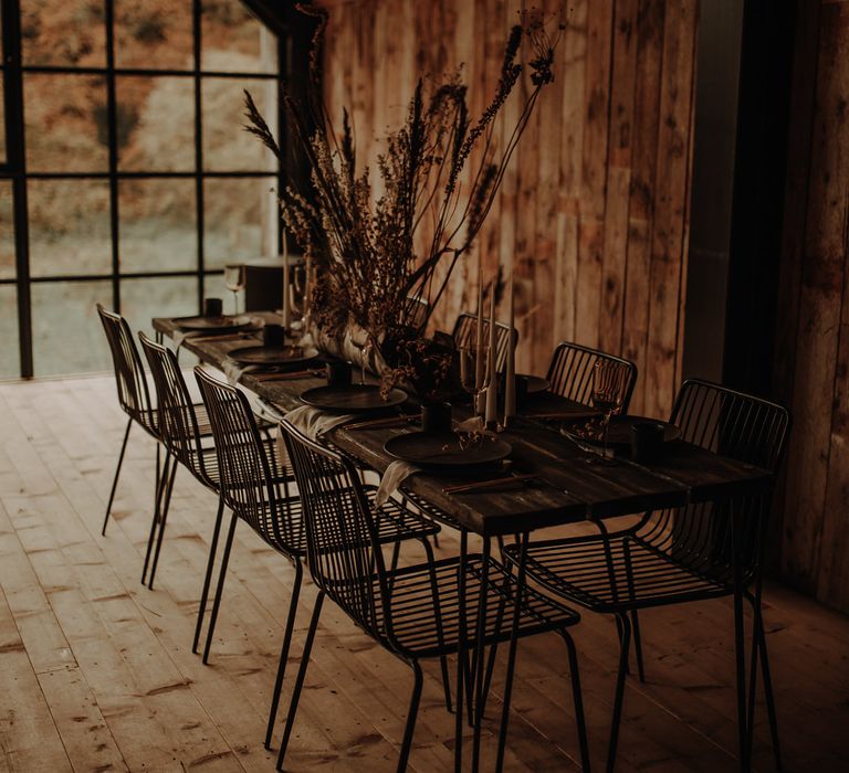 Intimate wooden tablescape with black wire chairs, dried flower centrepieces and taper candles decor 