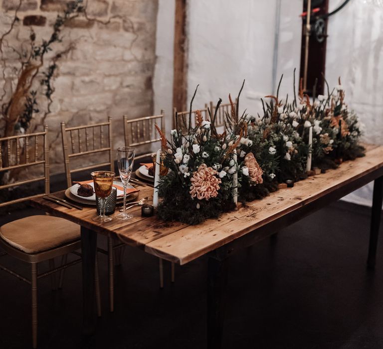 Chandelier light installation over a wooden table with orange flower and foliage table runner of flowers at Ponden Mill wedding venue 