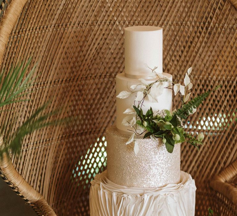 4-tiered wedding cake in white with ruffled decor and green foliage