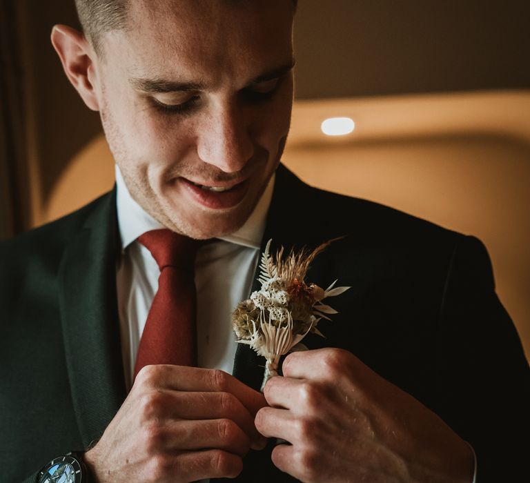 Groom pins dried floral buttonhole to suit on the morning of his wedding