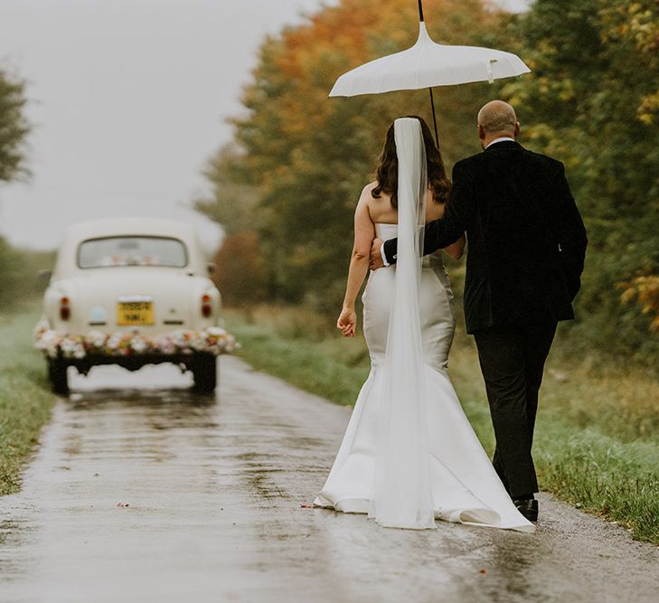 Groom in a velvet tuxedo jacket with his arm around his bride in a strapless fishtail wedding dress