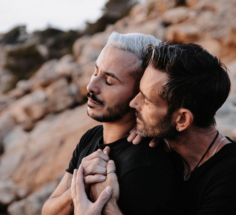 Grooms tenderly embrace as they hold one another's hands 