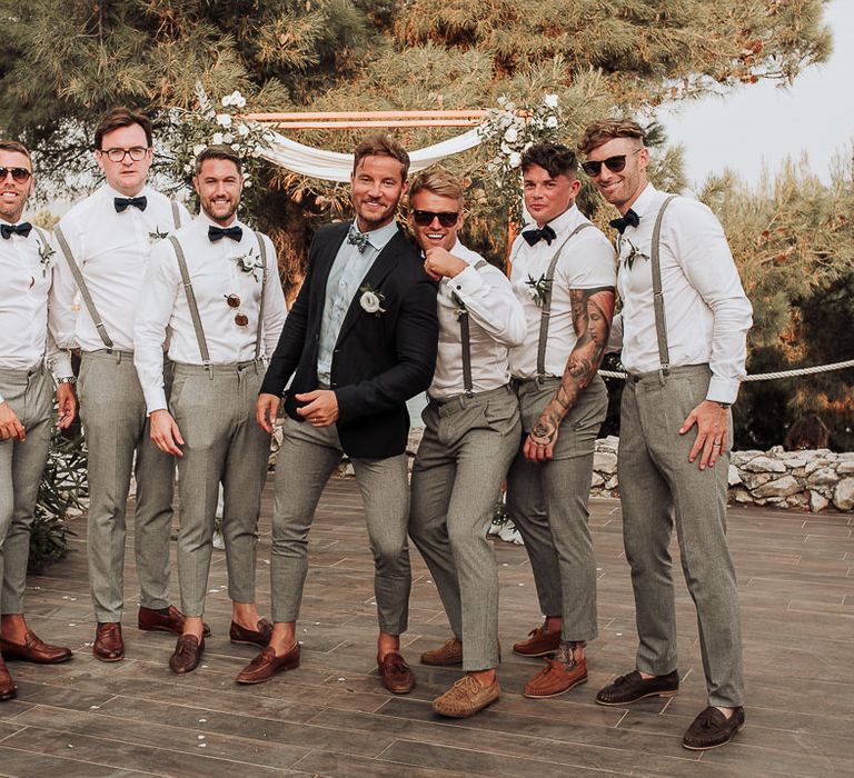 Groom in blue suit with groomsmen in matching white shirts and grey trousers