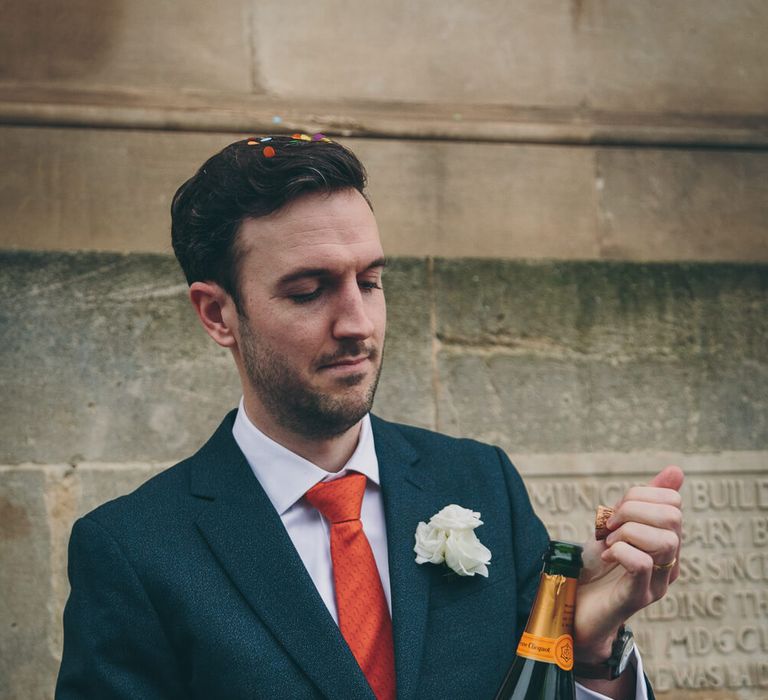 Groom wearing red tie opening a bottle of champagne 