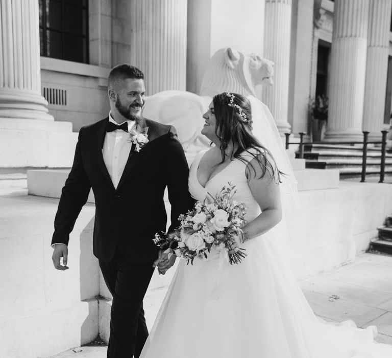 Bride & groom walk together through London as brides veil blows in the wind