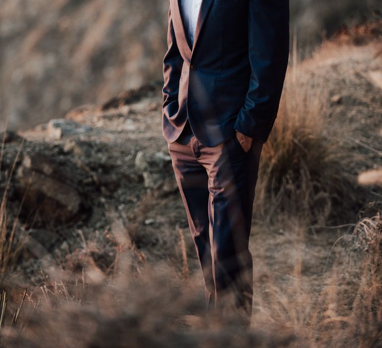 Groom wears blue suit with open shirt on the cliffside