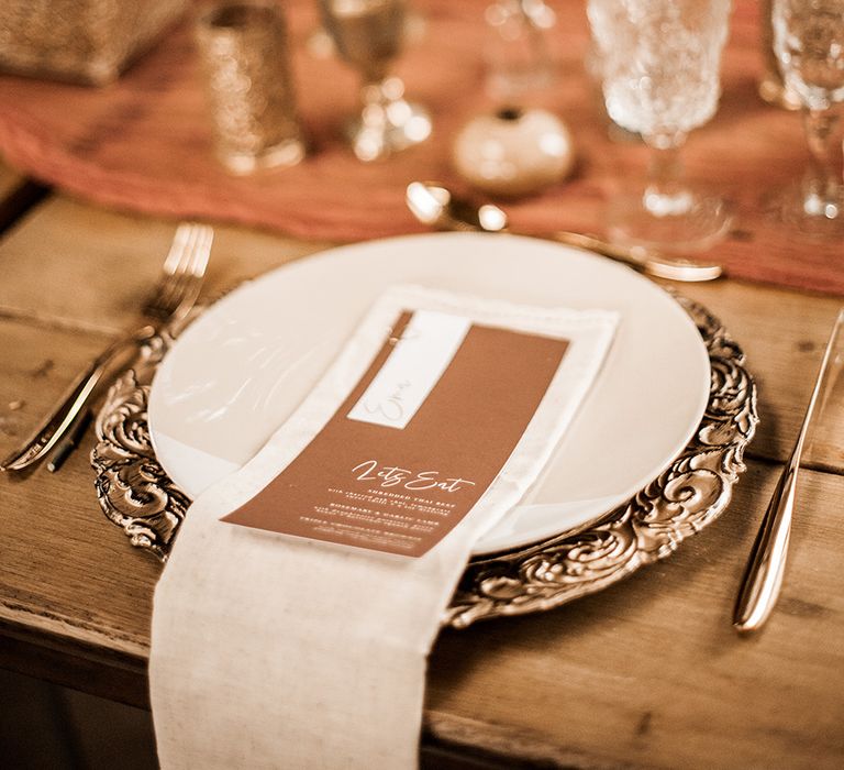 Place setting with gold charger place, gold cutlery and brown menu card 