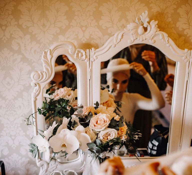 Bride gets ready at white vanity table with her white low-heeled wedding shoes on display with her Dolce and Gabbana perfume