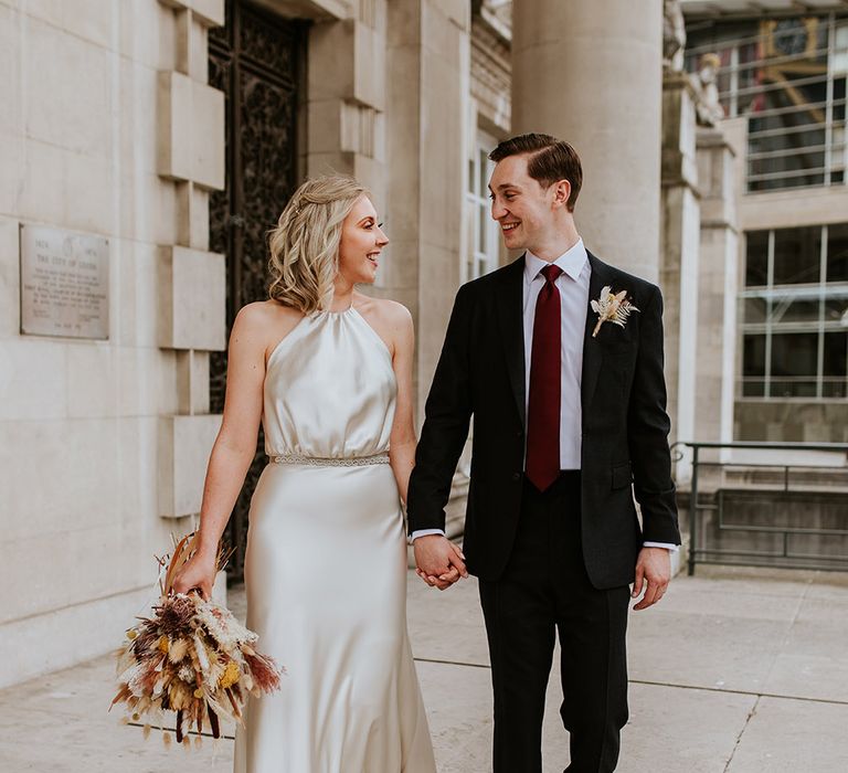 Stylish bride and groom in a halter neck, satin, champagne colour wedding dress and black suit 