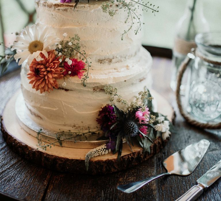 Rustic naked wedding cake complete with white frosting and floral decor