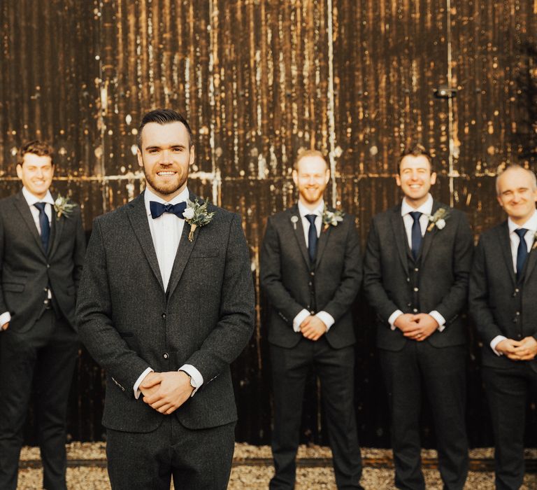 Groom and groomsmen in charcoal grey wedding suits with navy bow ties 