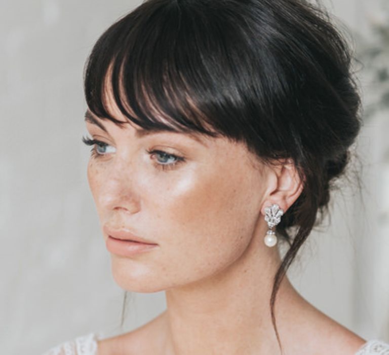 Brunette bride with a fringe and freckles with natural makeup and highlighter across her cheeks 