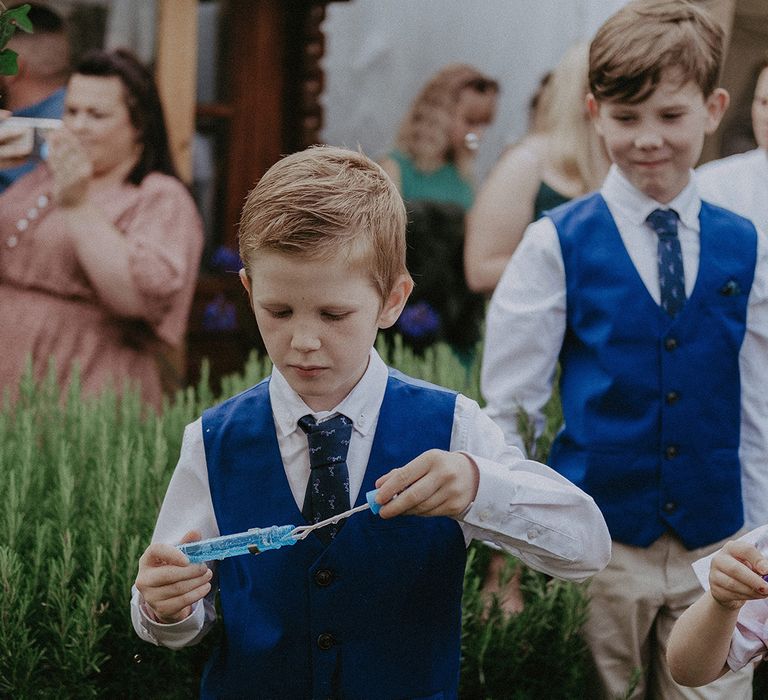 Page boys in blue waistcoats blowing bubbles 