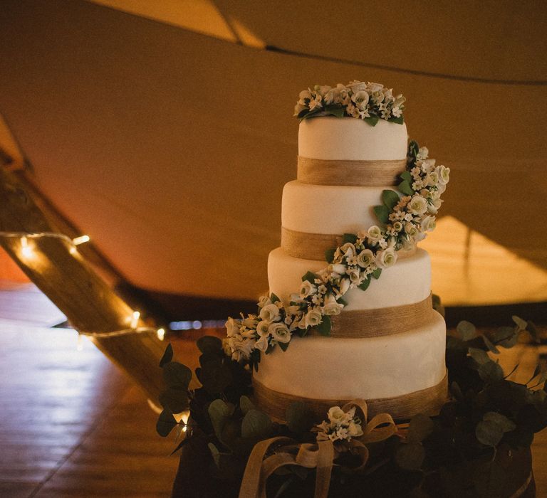 White four tier iced wedding cake with white rose garland and cake topper for tipi wedding at Inkersall Grange Farm