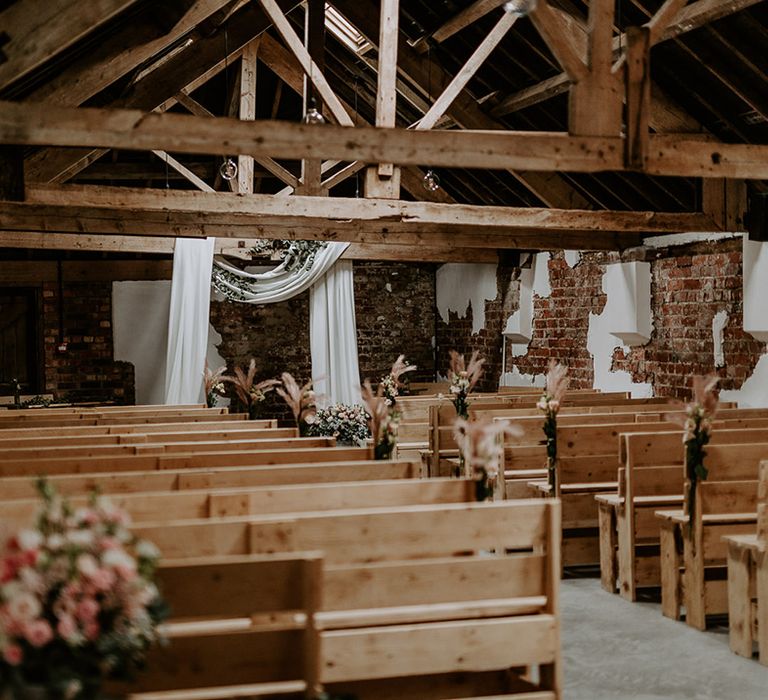 Woolas Barn wedding ceremony room with exposed brick, low beams, drapes and flowers decorating the aisle 