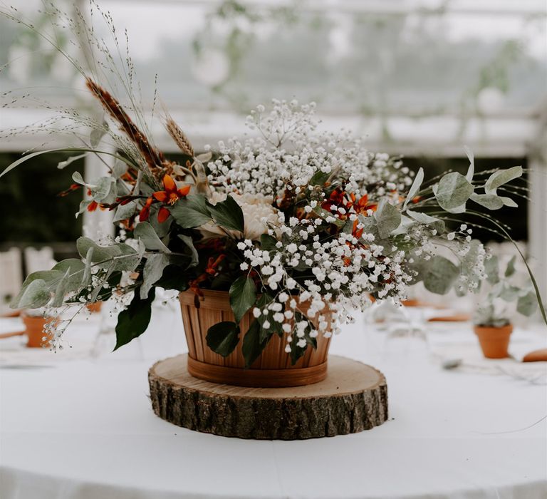 Wooden pot full of mixed white, red and green foliage on table at marquee wedding reception in Bedfordshire