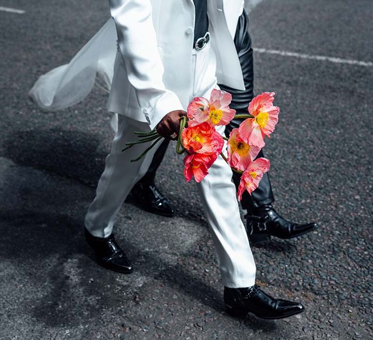 Groom in a white suit holding a bright red wedding bouquet 