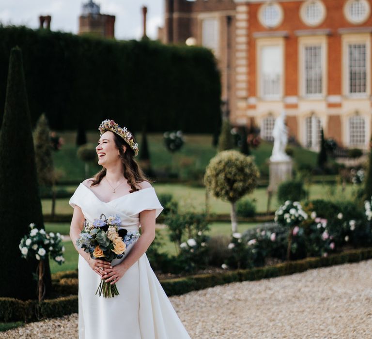 Bride stands outside Hampton Court Palace as she holds floral bouquet