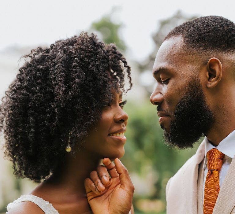 Intimate wedding portrait of groom holding his bride's chin with naturally curly hair and plunging neckline wedding dress