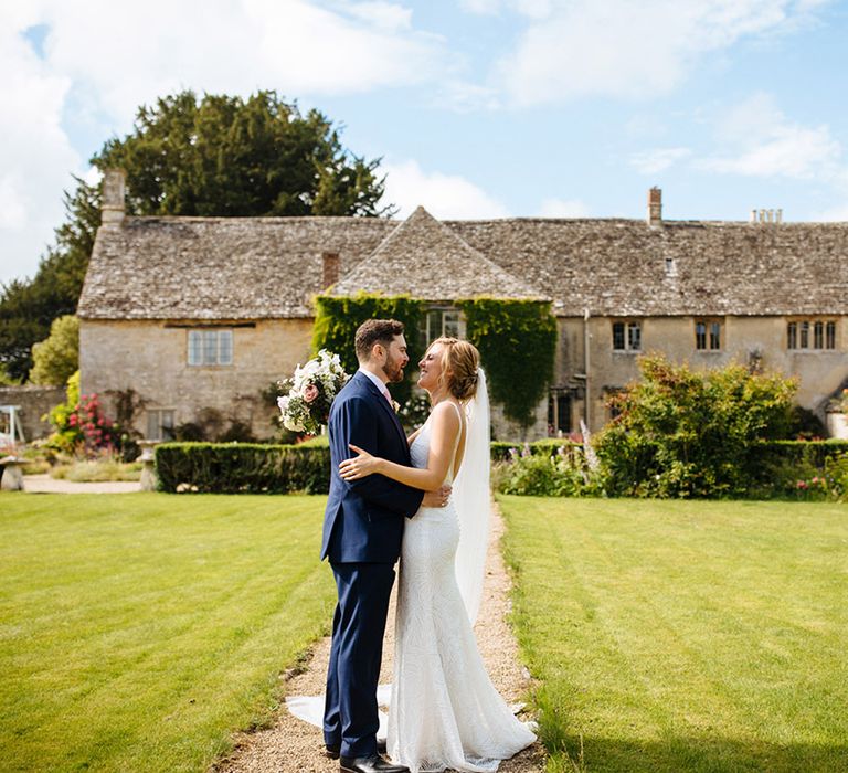 Bride in a Made With Love Bridal gown and groom in a navy suit standing in front of their Caswell House wedding venue 