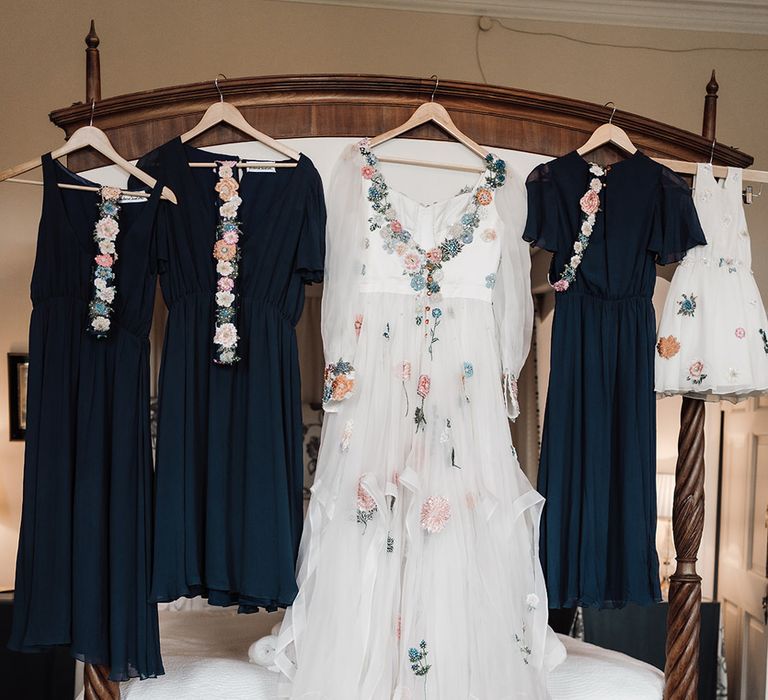 Long sleeve Victoria Sanders wedding dress with floral embroidery and train hung on four poster bed with navy bridesmaid dresses