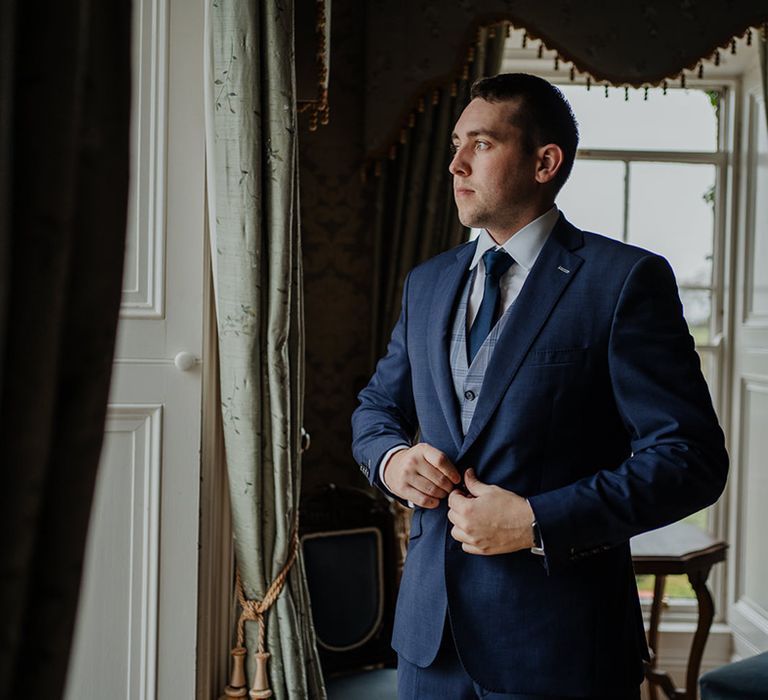 Groom in navy three piece wedding suit morning of the wedding at Horetown House