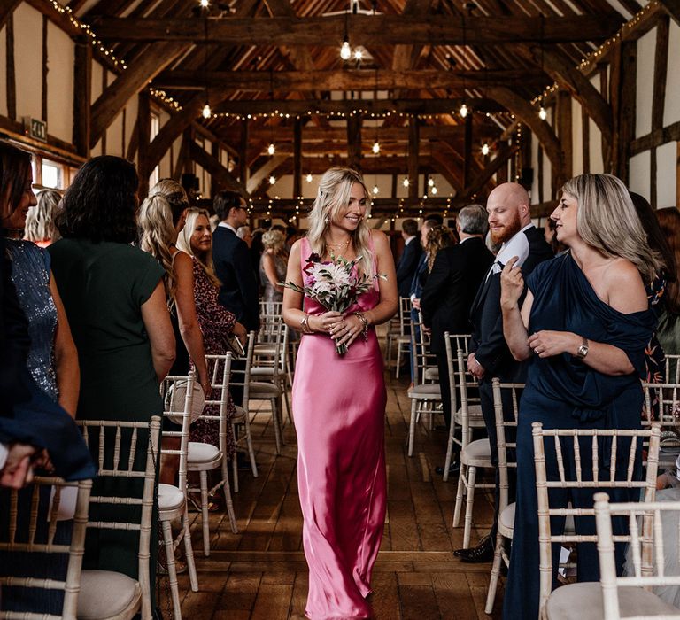 Bridesmaid walking down the aisle in a pink satin bridesmaid dress