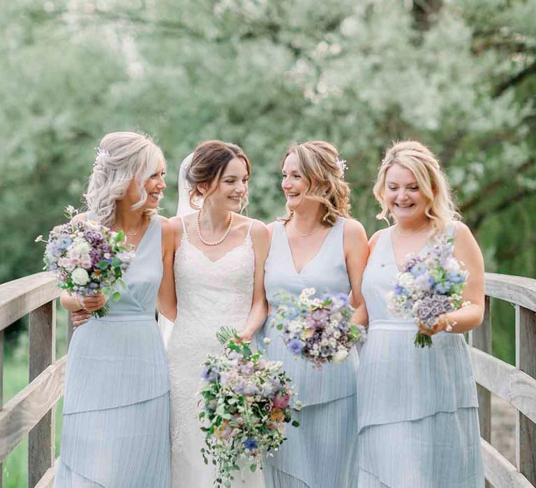 Bride stands with her bridesmaids who wear pale blue gowns 