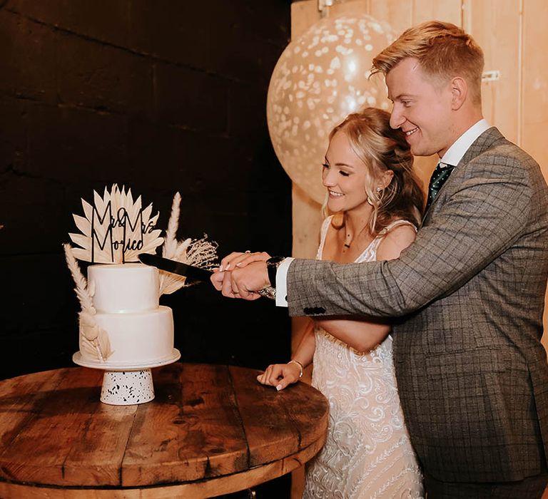 Bride and groom cut contemporary wedding cake with black personalised cake topper