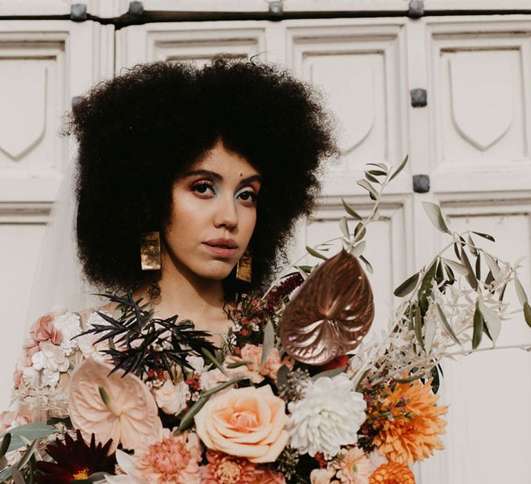 Black bride with afro hair holding a orange, peach, pink wedding bouquet with gold anthurium, dahlias and roses 