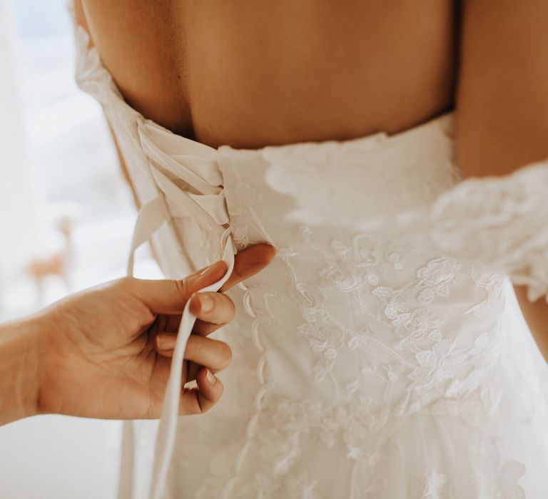 Bridesmaid does up the ribbons on bride's lace corset back wedding dress