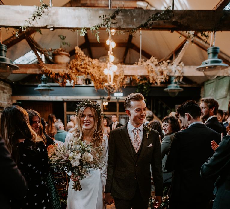 Bride walks with floral bouquet whilst wearing floral gown and satin wrap wedding dress