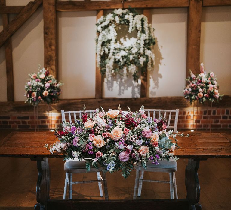 Dark wooden table with large flower displays of pink, white, orange and purple flowers at rustic country house venue