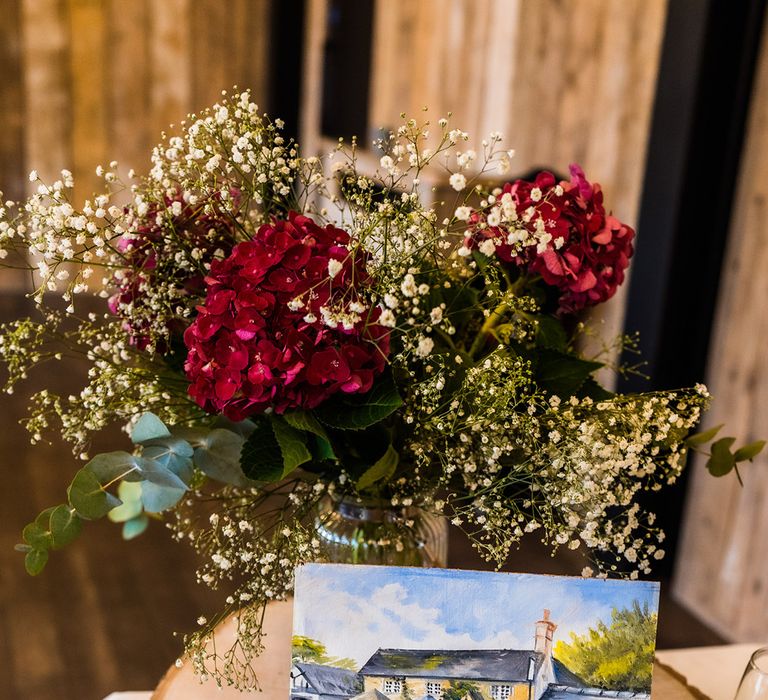 Tree trunk stand with hand-painted landscape with bunch of deep red hydrangeas and gypsophila