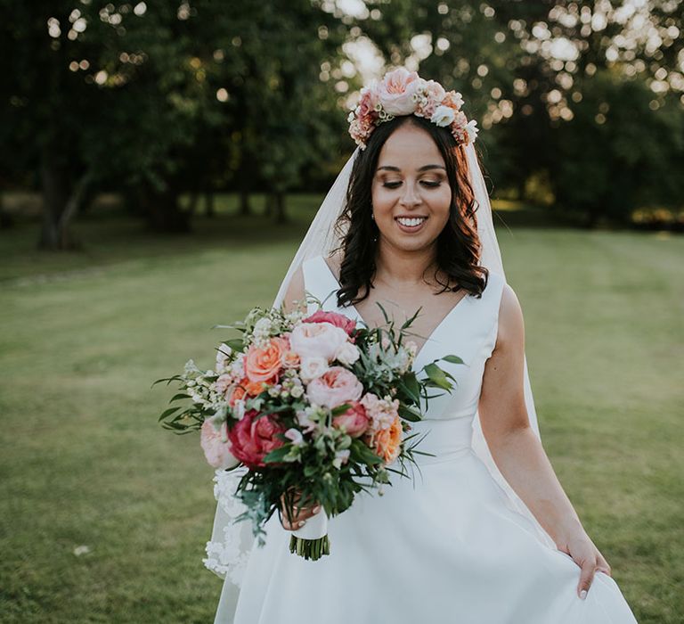 Bride holding pink, red and orange bouquet with large pink flower crown and v-neck Stella York wedding dress