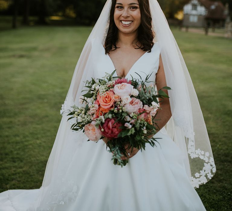 Beautiful smiling bride in Stella York wedding dress and Pronovias flower embroidered veil with pink flower crown