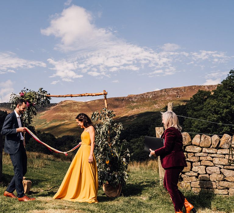 Outdoor wedding with handfasting ceremony and bride in a yellow wedding dress