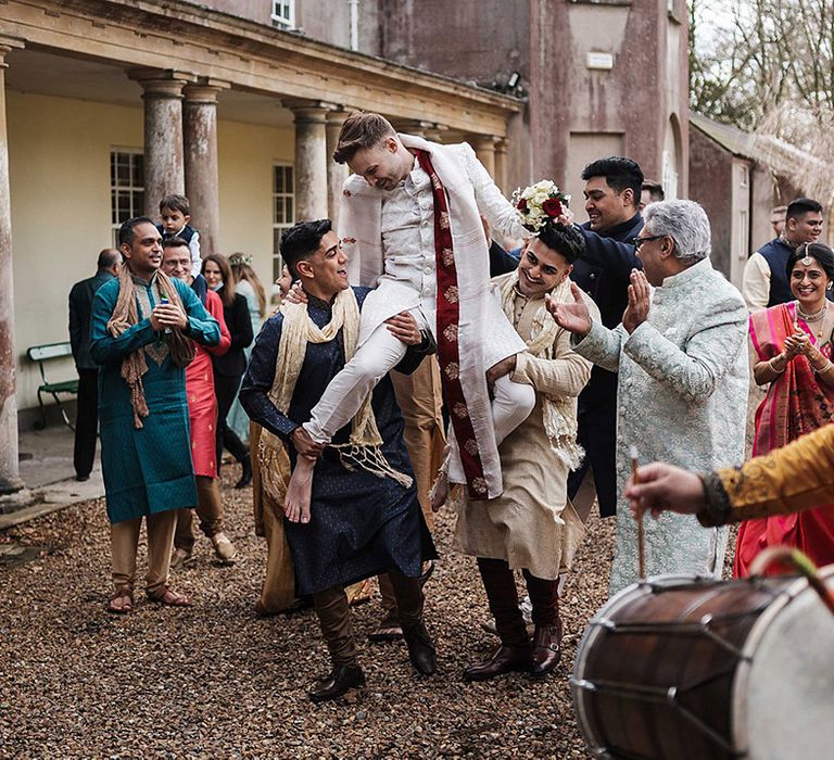 Groom is lifted up by wedding guests as a Dhol is played