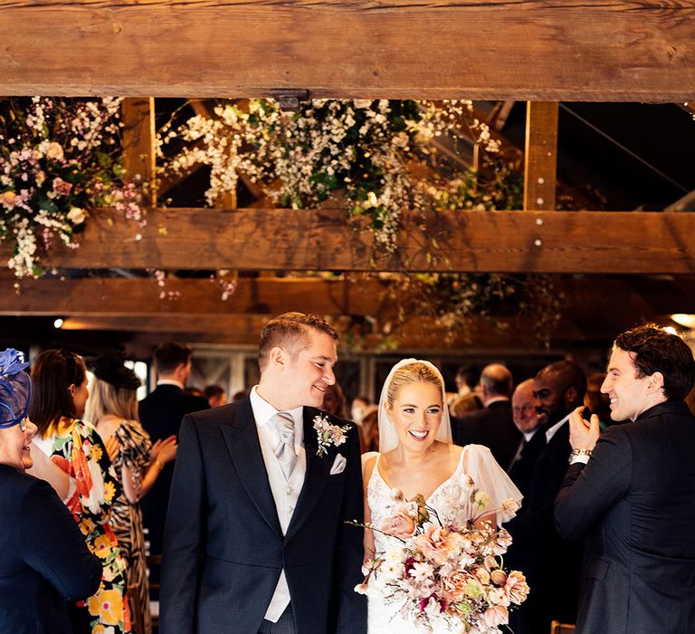 Groom in grey morning suit with pinstripe trousers smiles at the bride as they exit their wedding ceremony