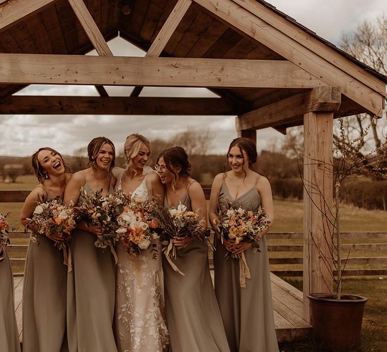 Bride laughs and smiles with her bridesmaids in green dresses outside Eden Barn wedding venue after the rustic barn wedding 