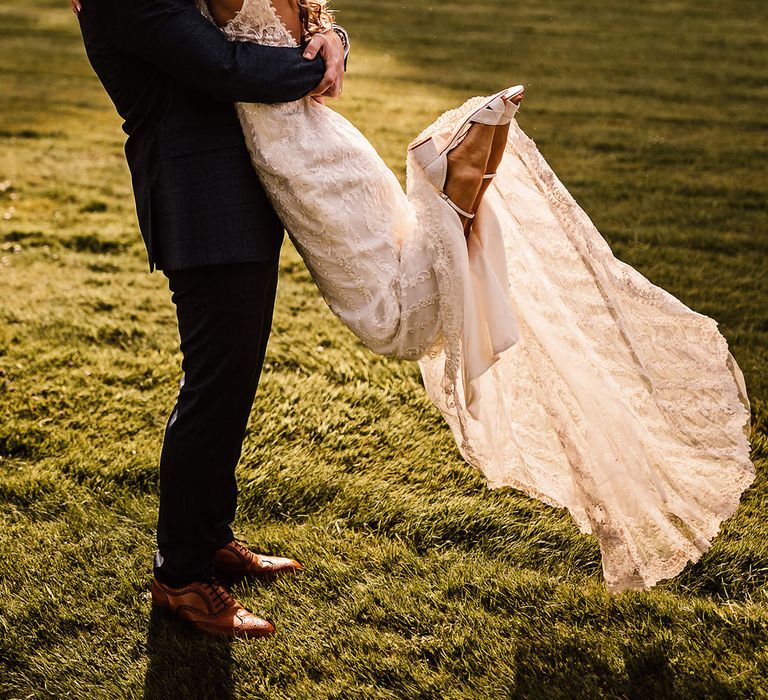 Groom in blue suit lifts the bride in a kiss with the bride wearing sparkly Charlotte Mills wedding shoes 