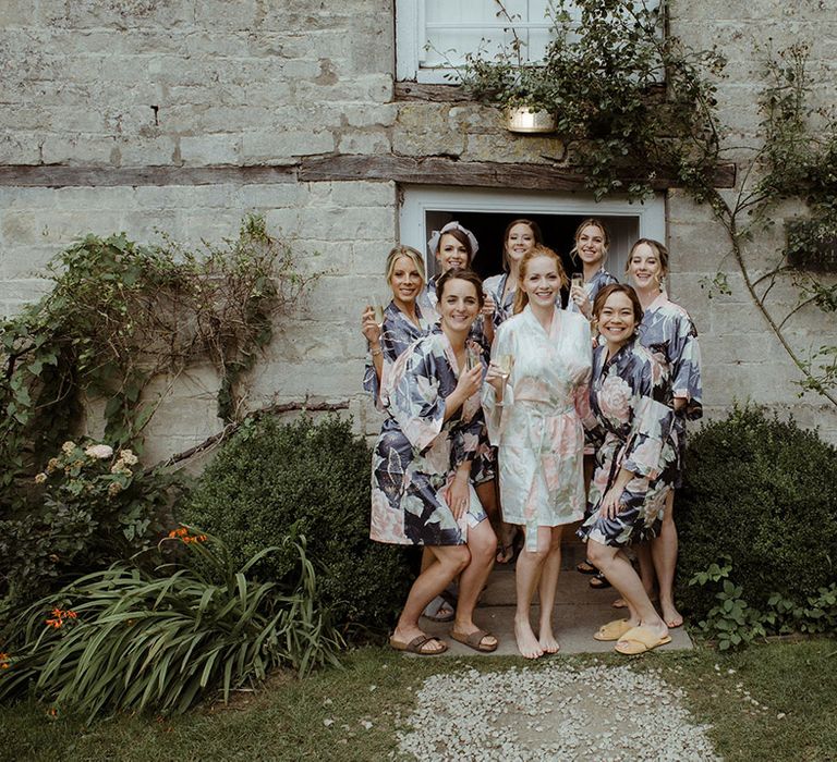 Bride in pastel pink and green floral satin robe with bridesmaids in darker blue floral satin robes for Owlpen Manor wedding 