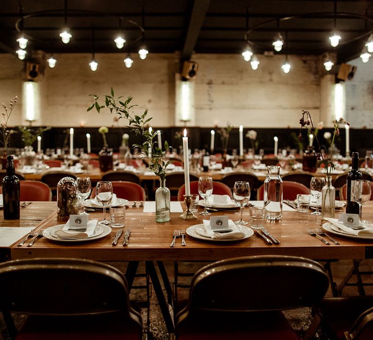 Wooden table complete with wine bottles filled with floral decor in rustic setting for reception 