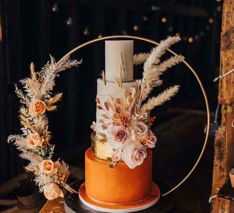 Orange, gold and white four tier wedding cake with roses and dried grass 