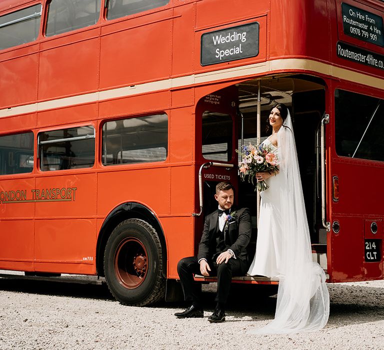 Bride and groom pose with their red double decker bus wedding transportation 