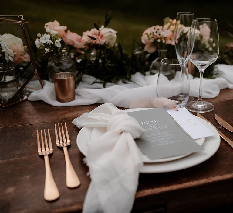 Place setting with white tableware, gold cutlery and grey menu card 