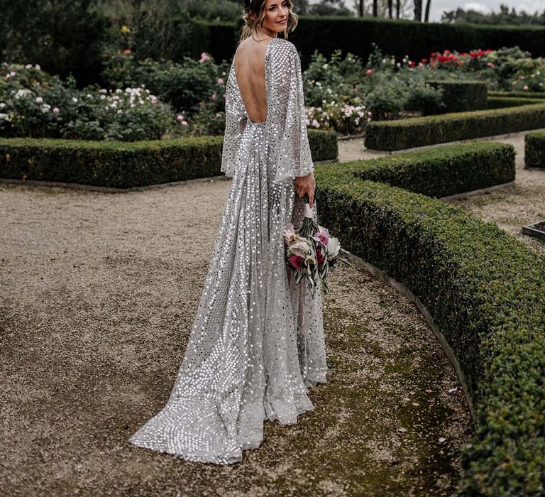 Bride wears silver sequin wedding dress with low back and bridal crown whilst holding colourful floral bouquet 