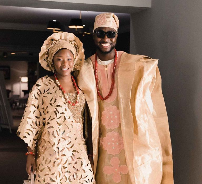 Bride wears intricately designer Nigerian dress with colourful embellishment and bold jewellery alongside her groom in sunglasses and Nigerian dress